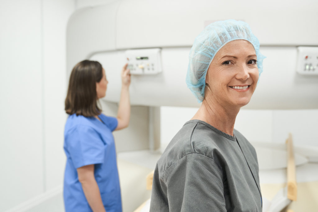middle aged patient in a hospital gown and cap with nurse behind her